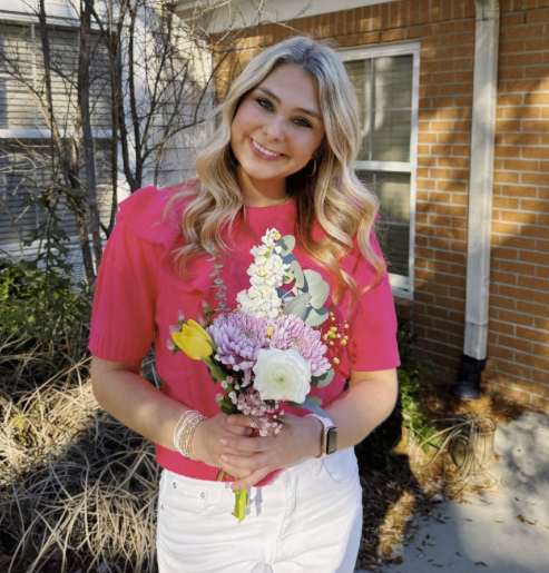 candid photo of education club president holding a bouquet of flowers in front of a building